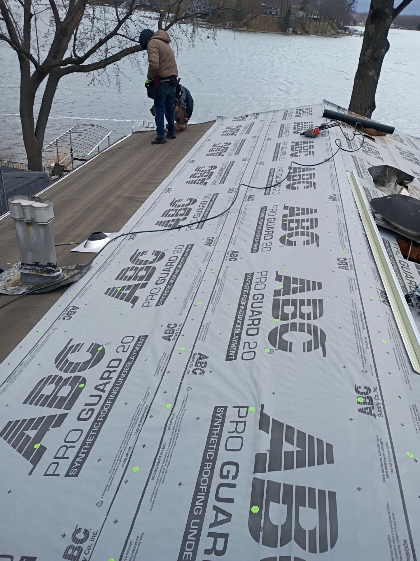 A worker installs roofing underlayment on a lakeside home, with a view of the water in the background.