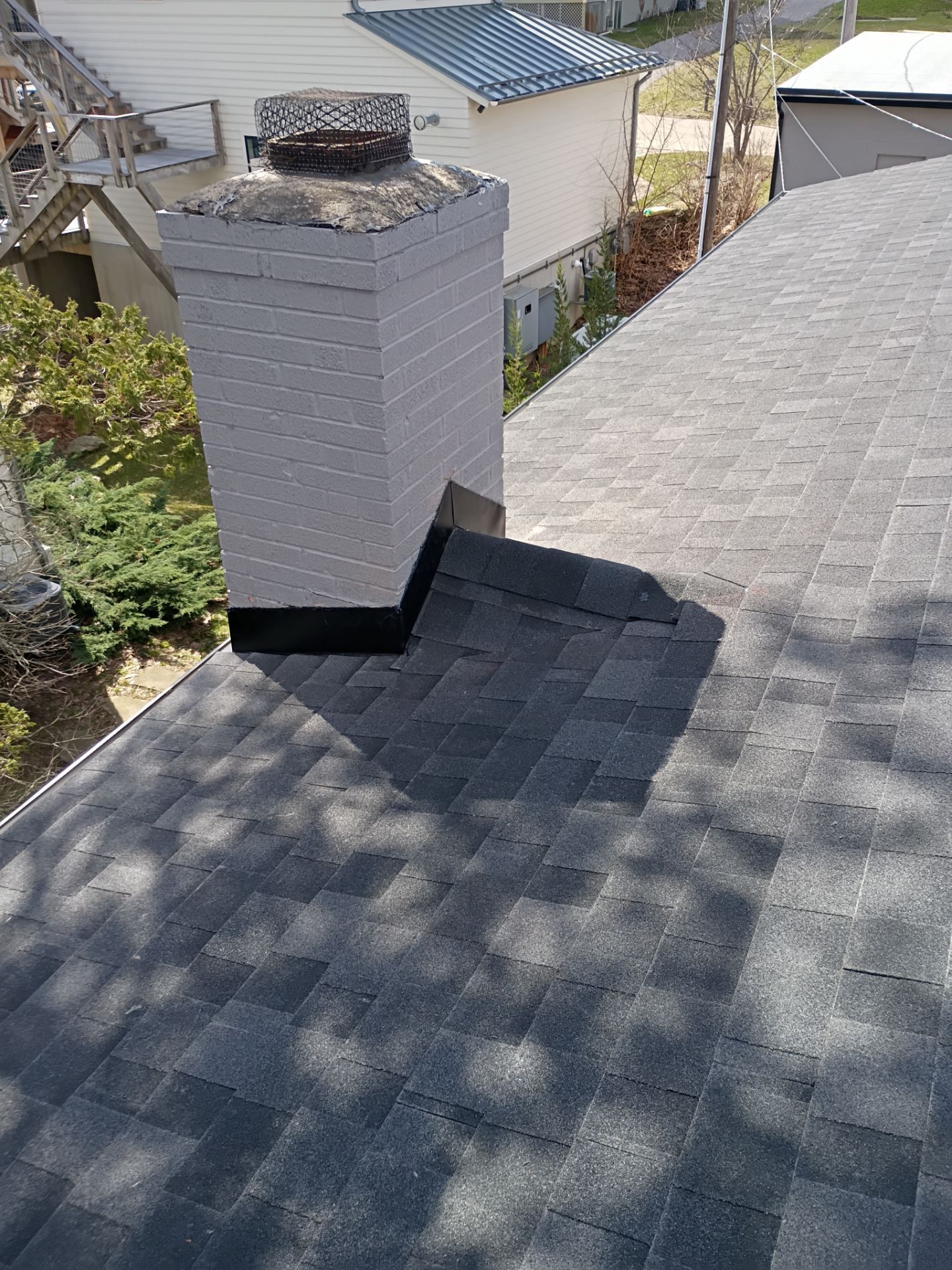 A gray brick chimney on a shingled roof with dark flashing installed at the base where it meets the roofline.