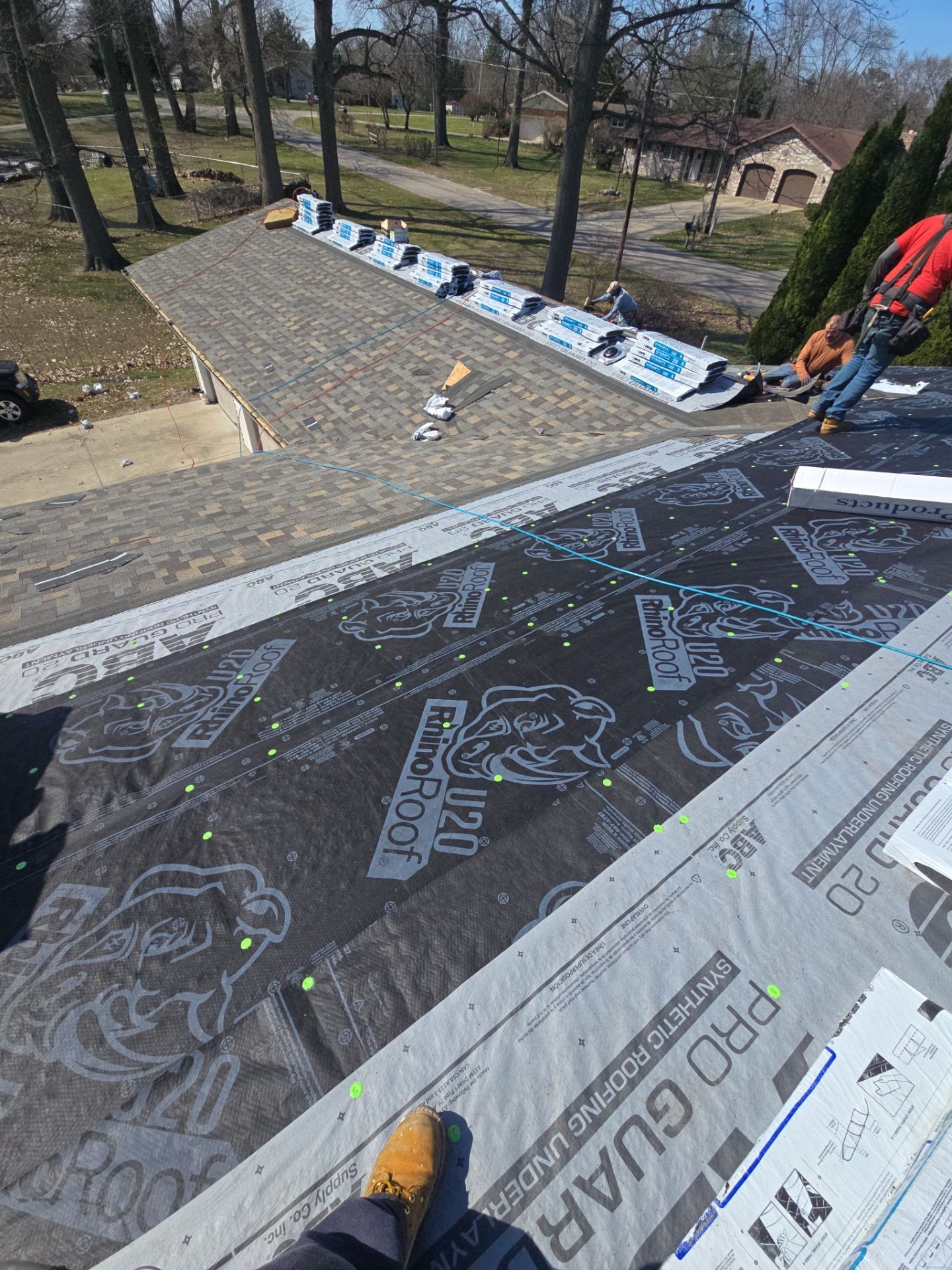 A construction worker stands on a partially shingled residential roof covered in ProGuard underlayment.