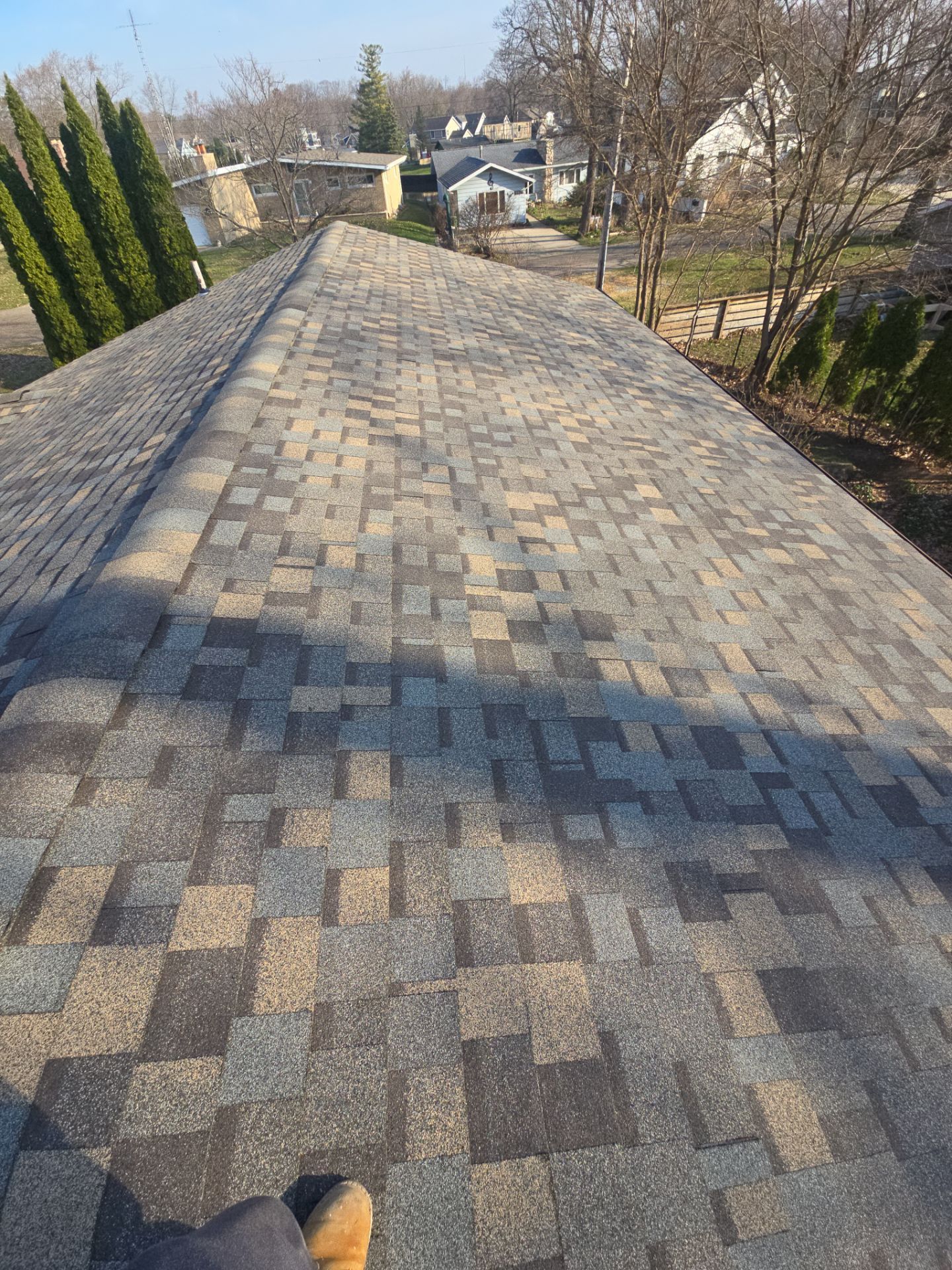 A high-angle view looking down the sloped, shingled roof of a house towards a residential street and trees.