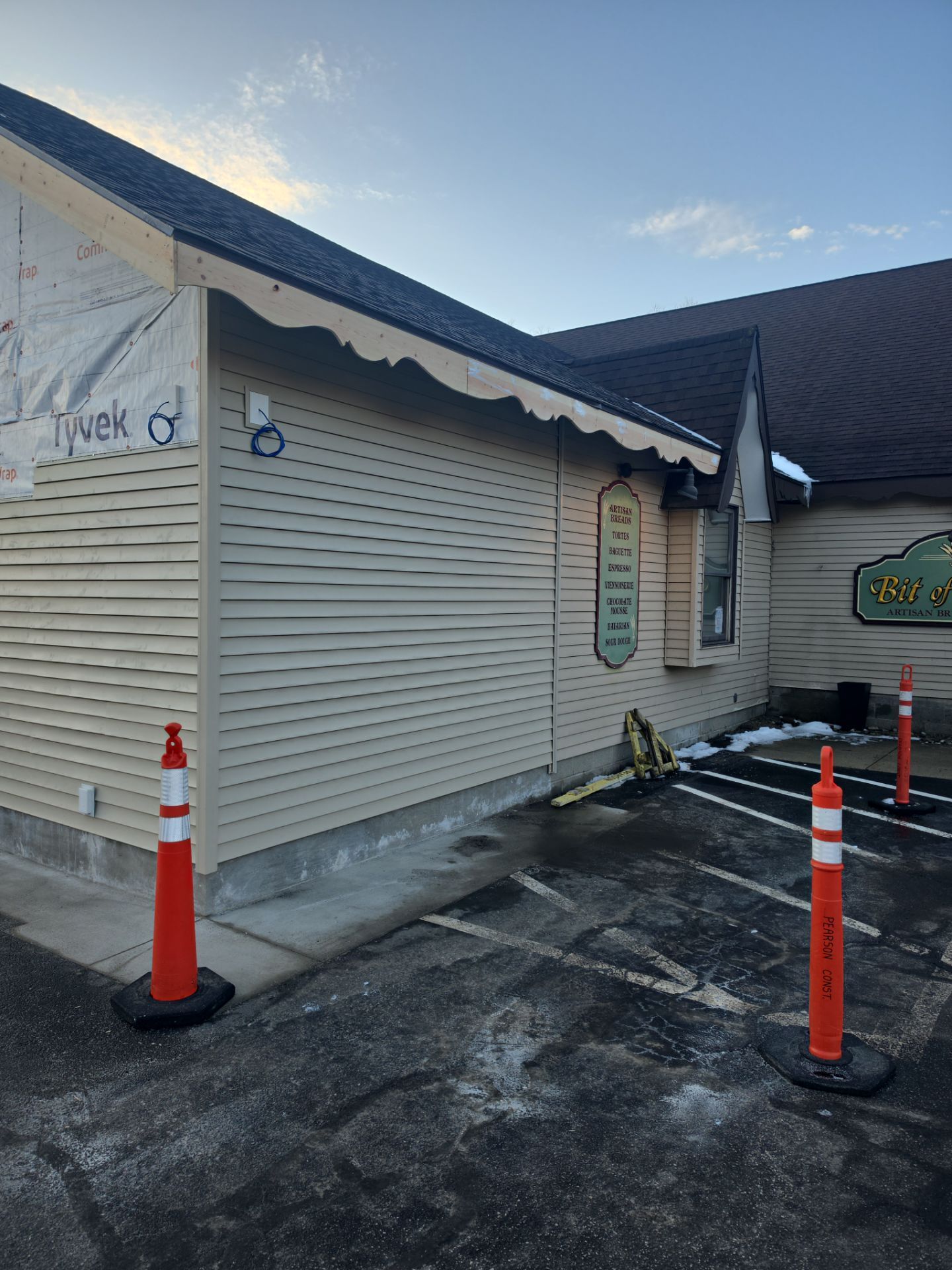 Side view of a beige building exterior under construction, with orange traffic cones in an asphalt parking lot.