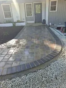 Brick paved walkway curves to a house entrance with a dark brick border and gravel edging.