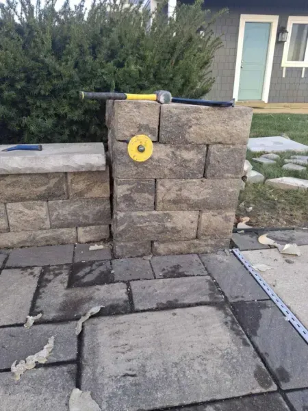 Stone pillars with a hammer and grinding wheel, near a house with a blue door.