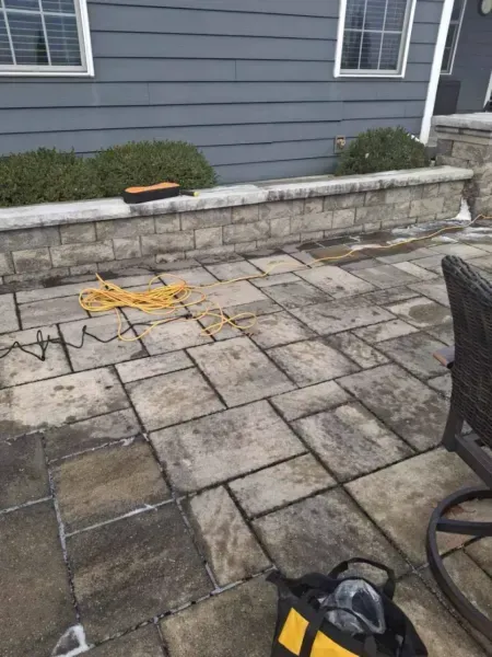 Patio with stone pavers, retaining wall, yellow extension cord, and tools near a house.