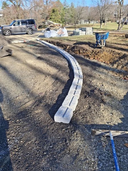 A curving stone curb under construction along a driveway, with tools and materials nearby.