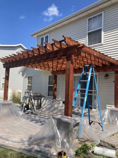 Newly stained wooden pergola attached to a house, blue ladder propped against the structure.