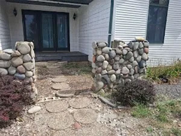 Stone pillars frame a pathway of stepping stones to a house entrance.