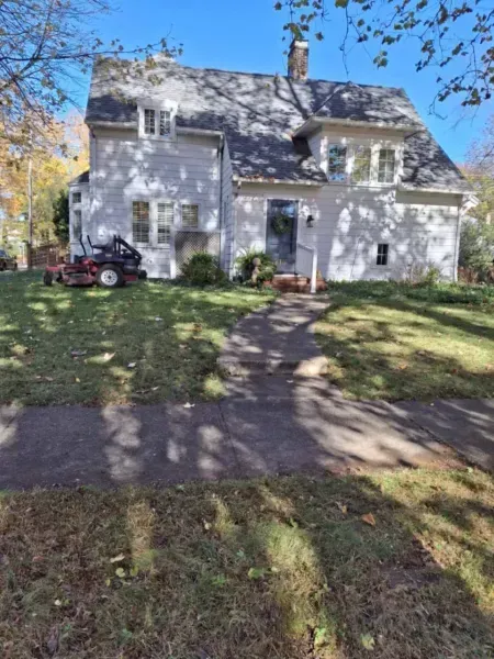 White house with a dark gray roof, lawn mower, blue sky.