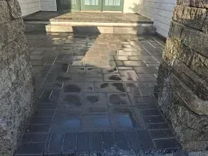 Wet, dark brick walkway leading to a doorway, flanked by stone pillars.