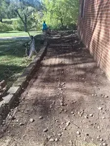 Dirt path next to a brick wall, bordered by a low brick wall on the left. Person in blue in the background.