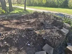 A circular garden bed with dirt, rocks, and paving stones on a sunny day near a road.