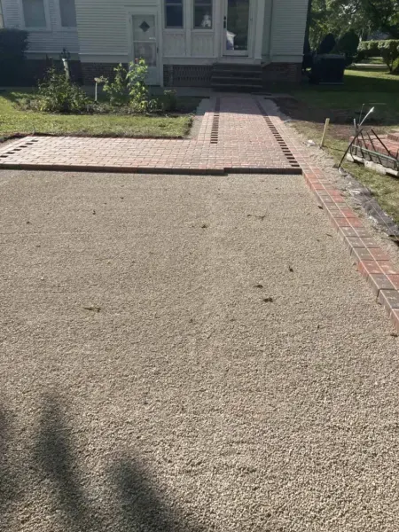 A gravel driveway with brick edging leads to a house with a brick pathway.