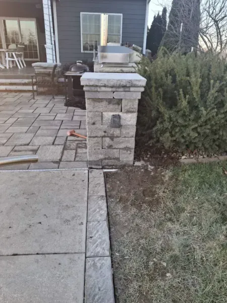 Stone pillar on patio with concrete border and grassy area.