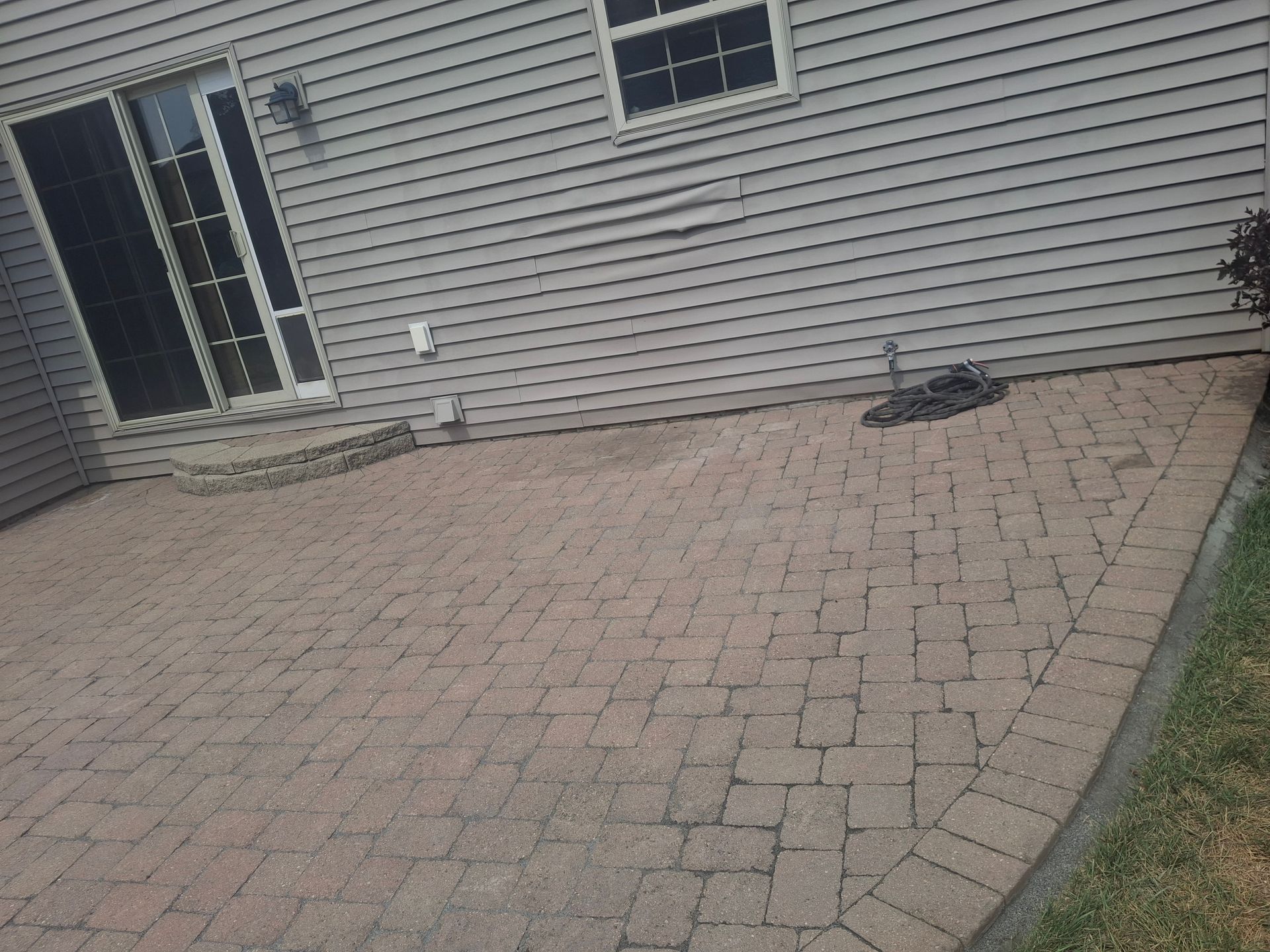 Brick patio outside a house with a sliding door and a small window.
