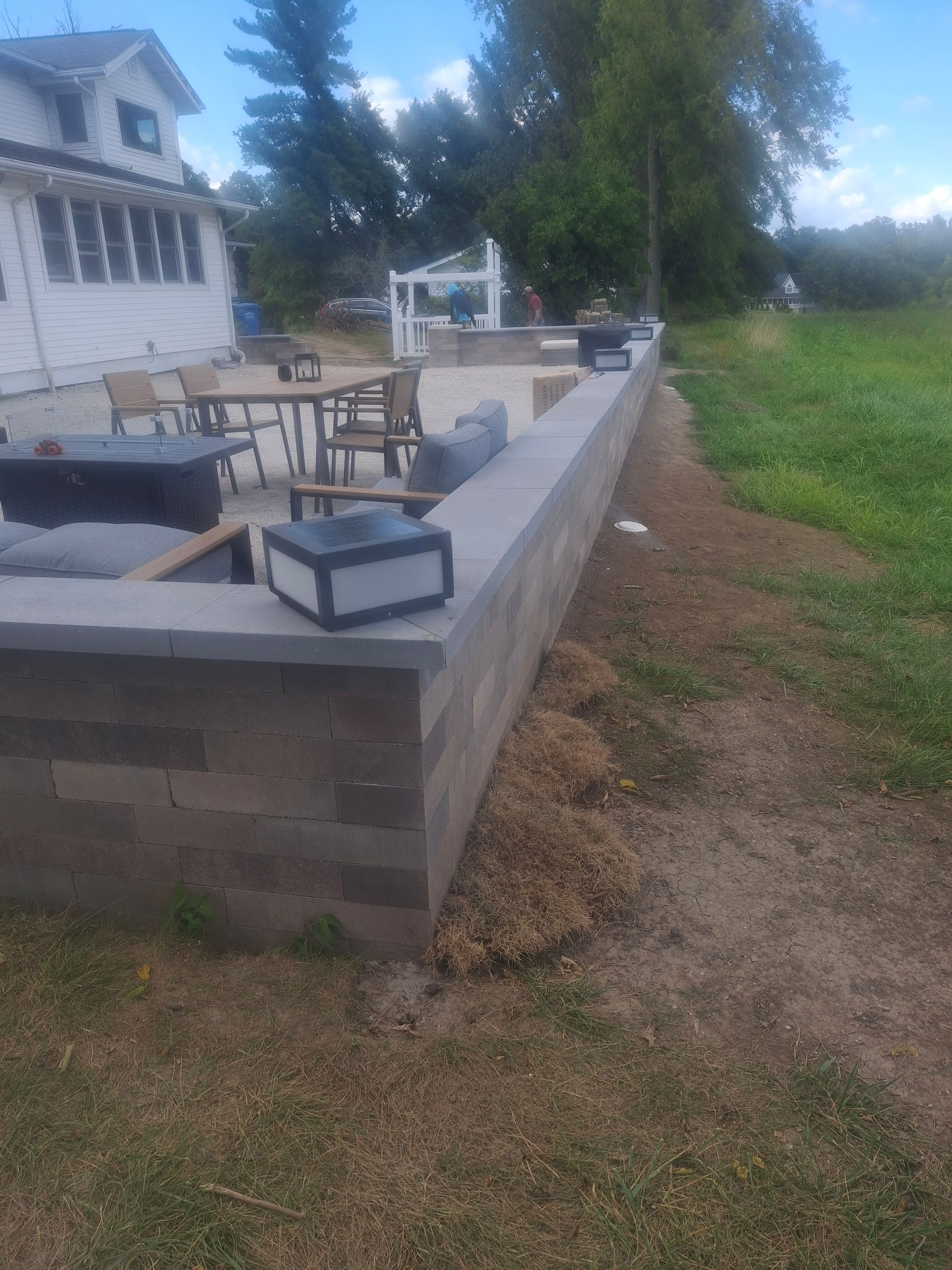Outdoor patio with a retaining wall, lawn furniture, and a grassy field.