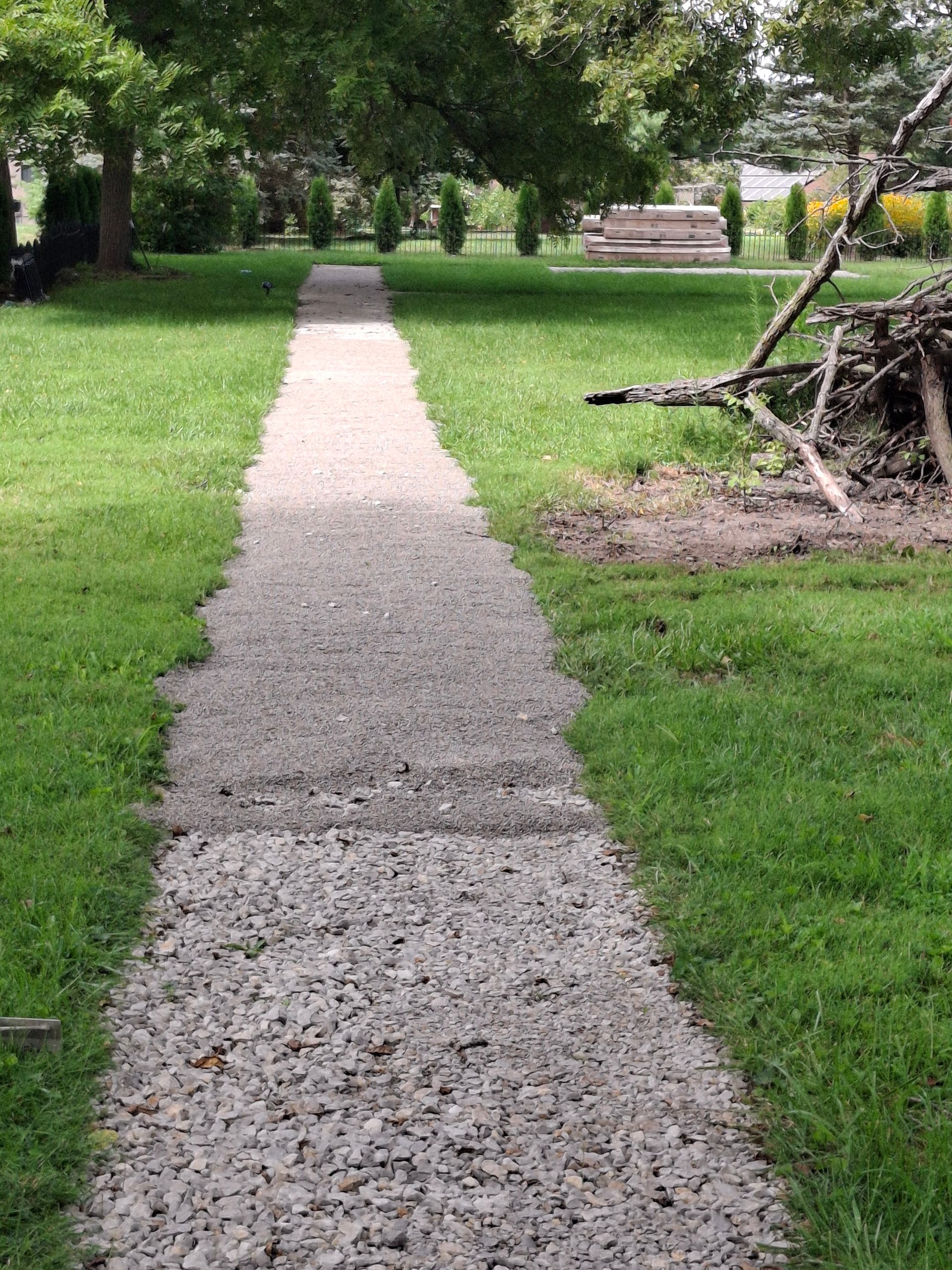 Gravel path through green grass, leading toward trees in a park-like setting.
