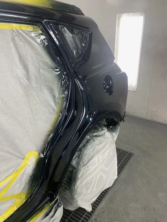 Car door frame being painted black in a paint booth. Masking tape and plastic protect nearby areas.
