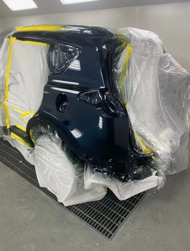 Car's rear quarter panel freshly painted dark blue, masked with plastic and tape in a spray booth.