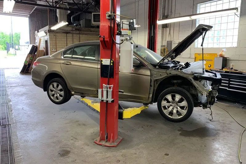Car on a lift in a garage with the hood open, front bumper removed.