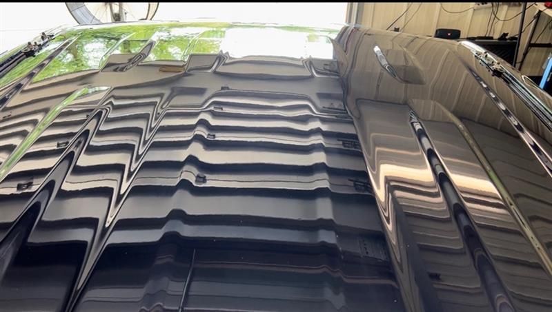 Glossy black car roof reflecting tree shadows and a tiled ceiling in a garage