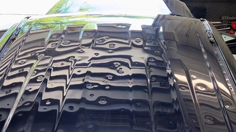 Close-up of a glossy black car hood with a wavy reflective surface.
