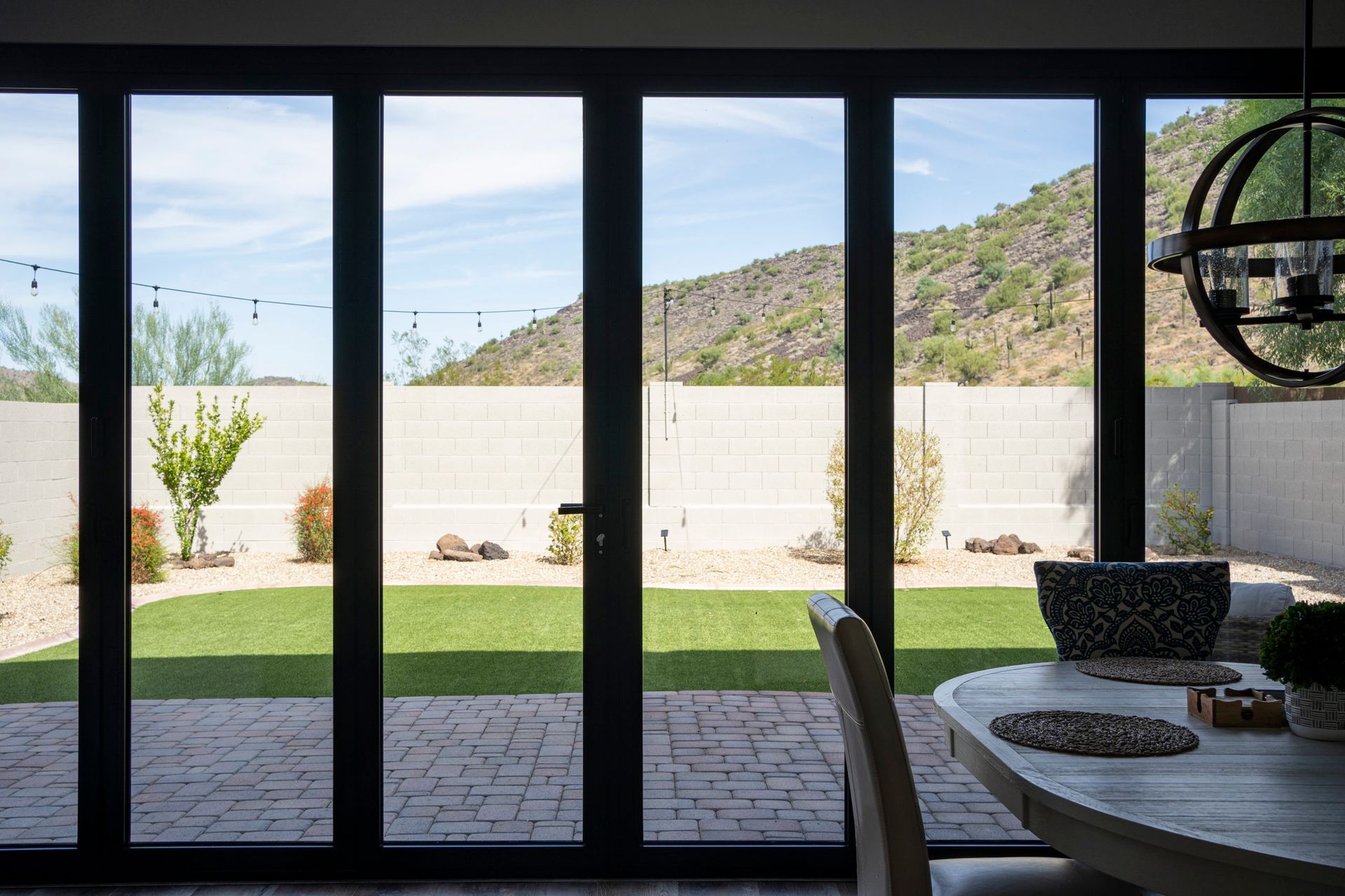 A black-framed, multi-panel door provides a view of a desert backyard with green grass, a stone wall, and a mountain in the distance.