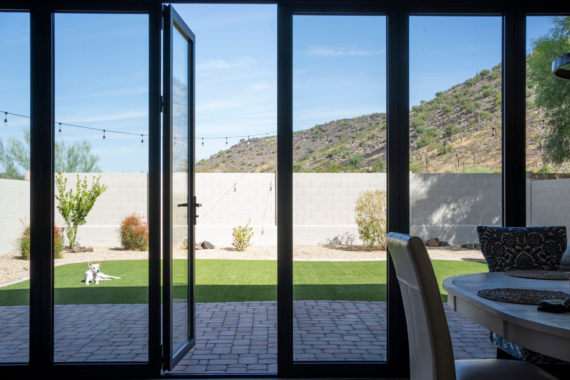 Open doors reveal a sunny backyard with a green lawn, brick patio, and mountain views.