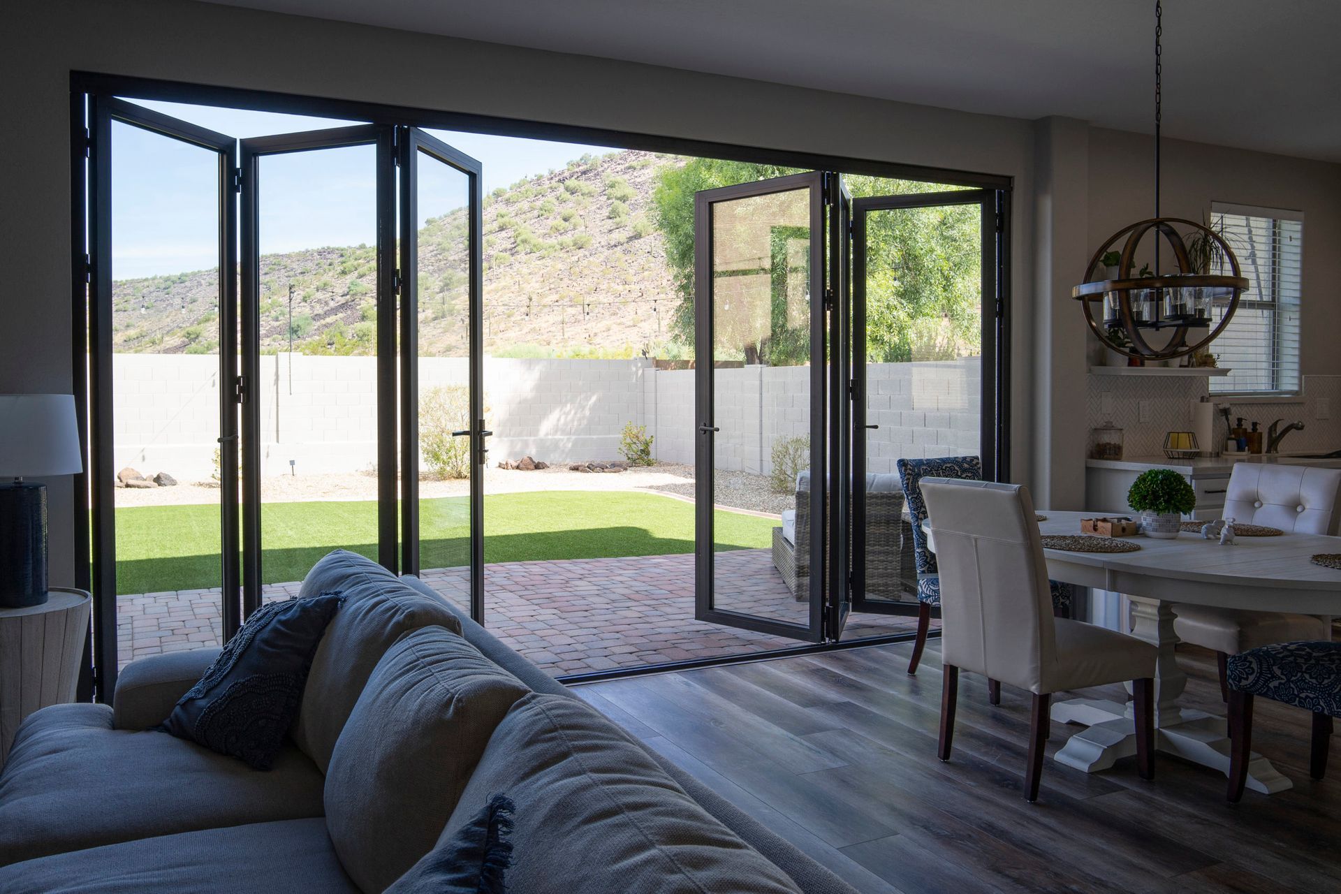 Living room with folding glass doors open to a backyard, view of lawn and mountains.