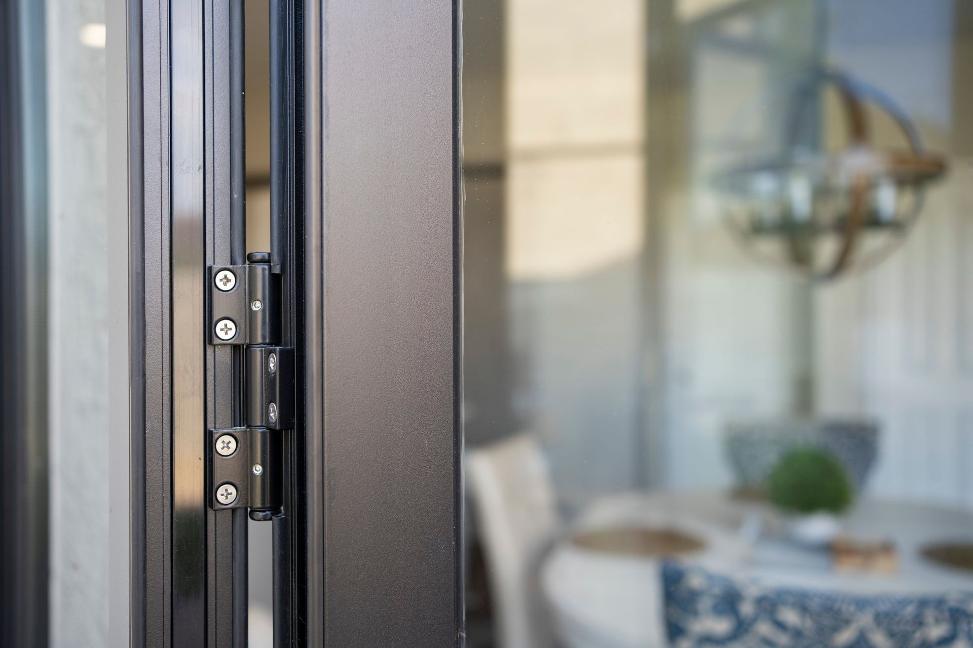 Black door hinge on a glass door, blurred interior dining setting visible.