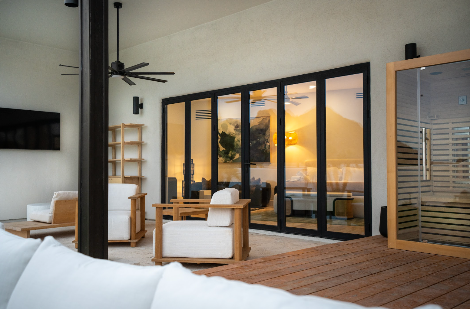 Modern patio lounge with white chairs, wooden deck, and sunset view through glass doors