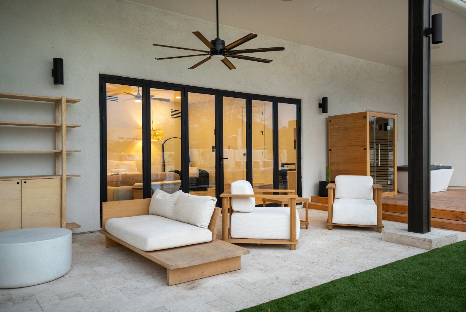 Modern patio with wicker seating, ceiling fan, glass doors, and warm indoor lighting