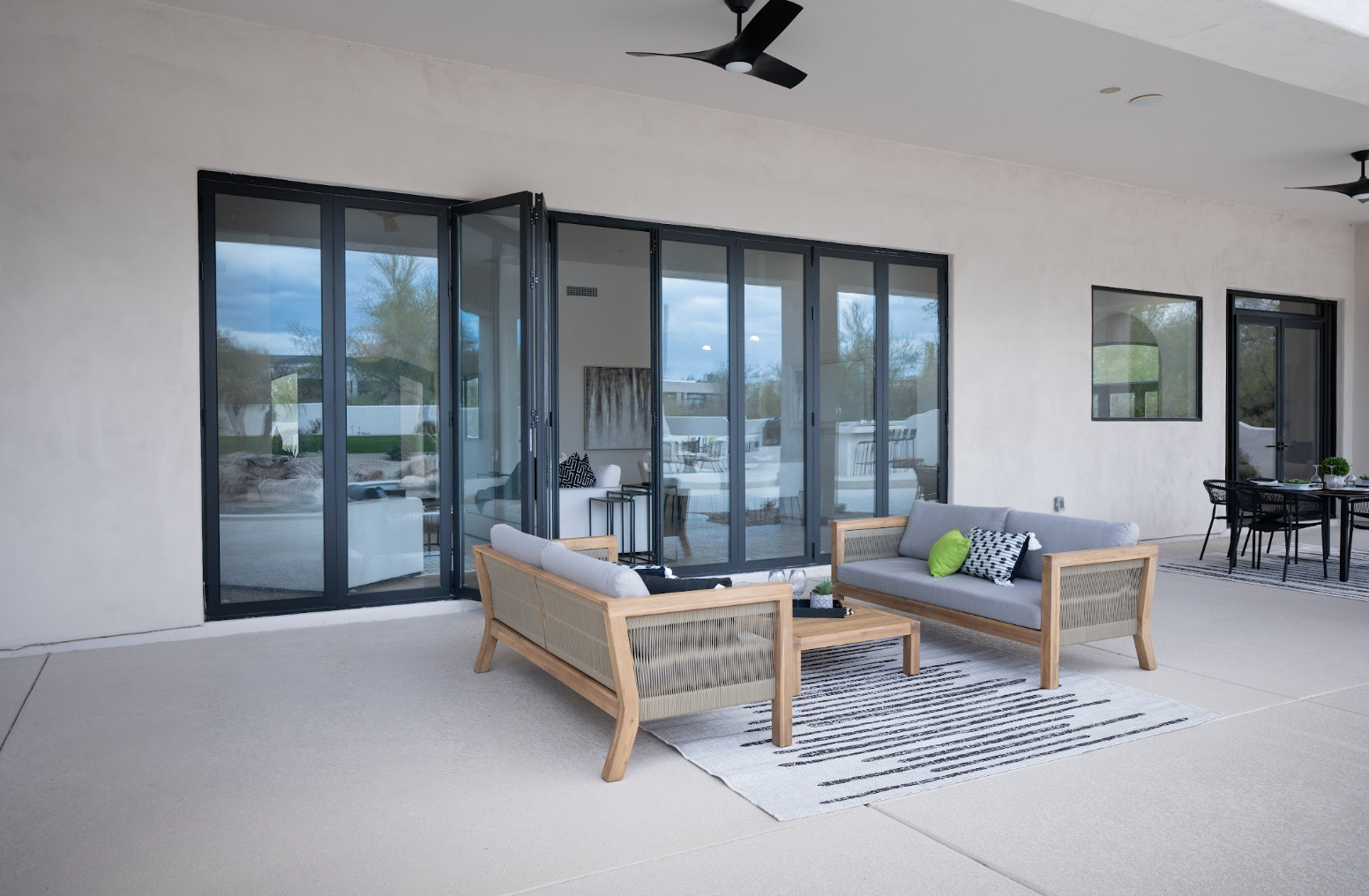 Outdoor patio with black-framed glass doors, wicker seating, rug, and dining table on a covered terrace