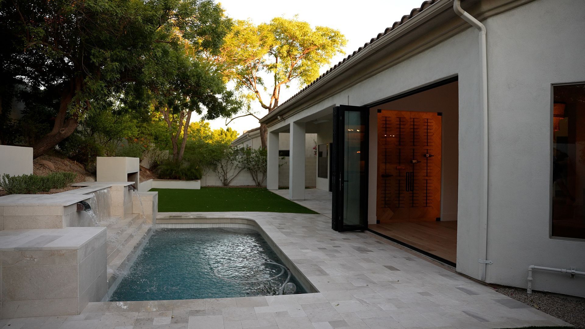 Modern patio with a small pool beside a white house and open glass doors at sunset