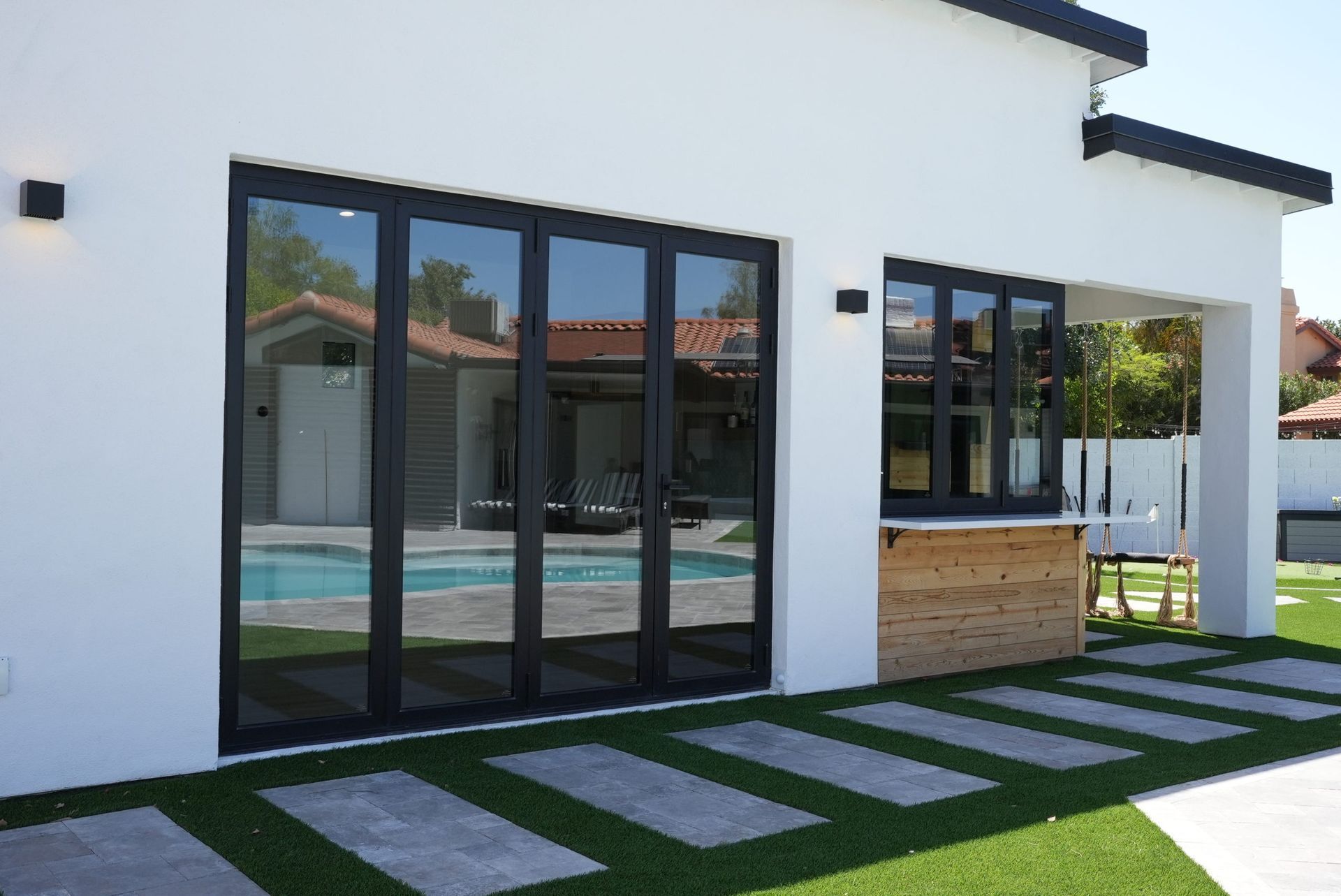 Modern white house patio with black-framed glass doors, a small pool, and stepping stones on green grass