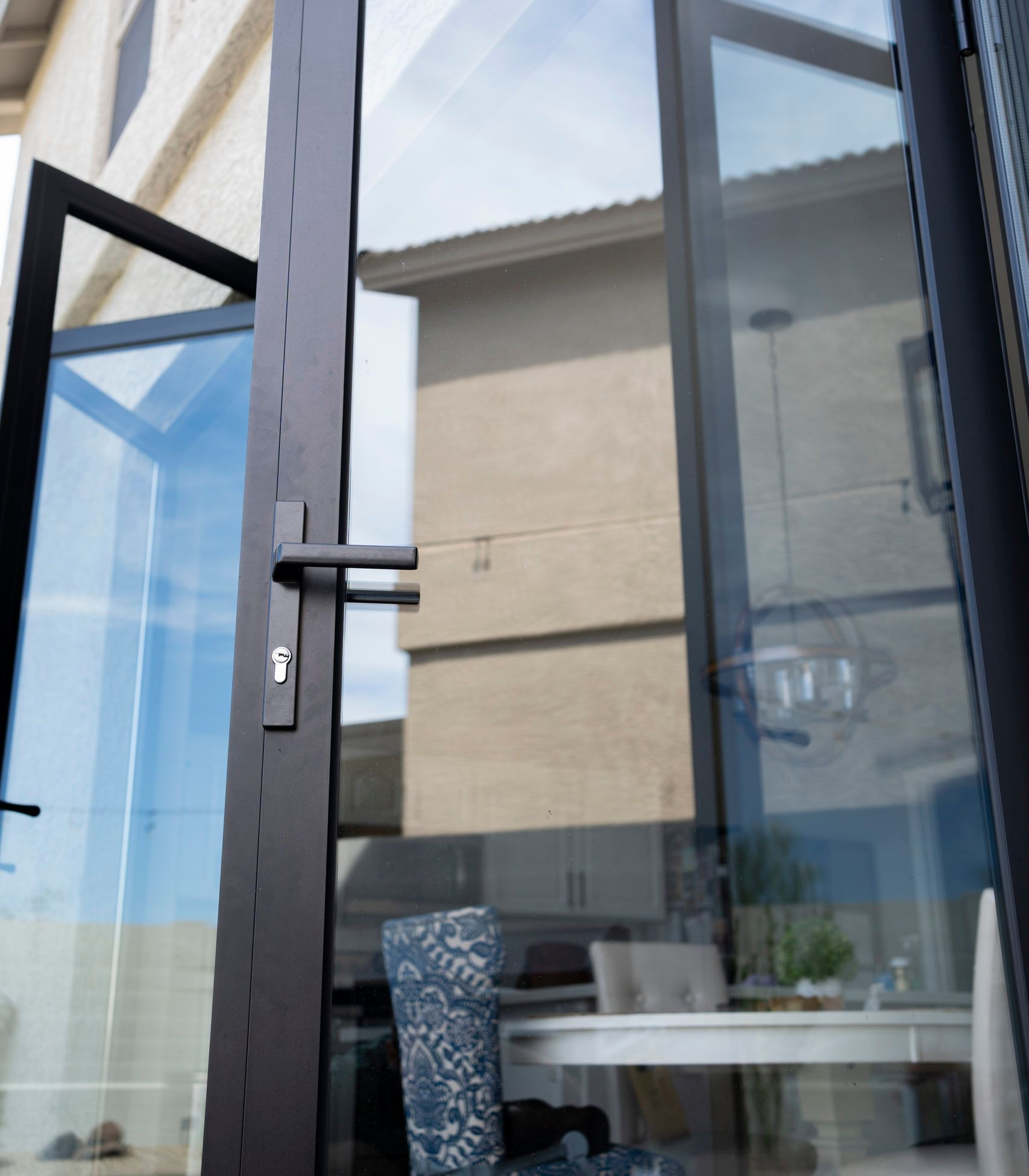 Open glass door to a patio with a table, chair, and beige building reflected in the glass