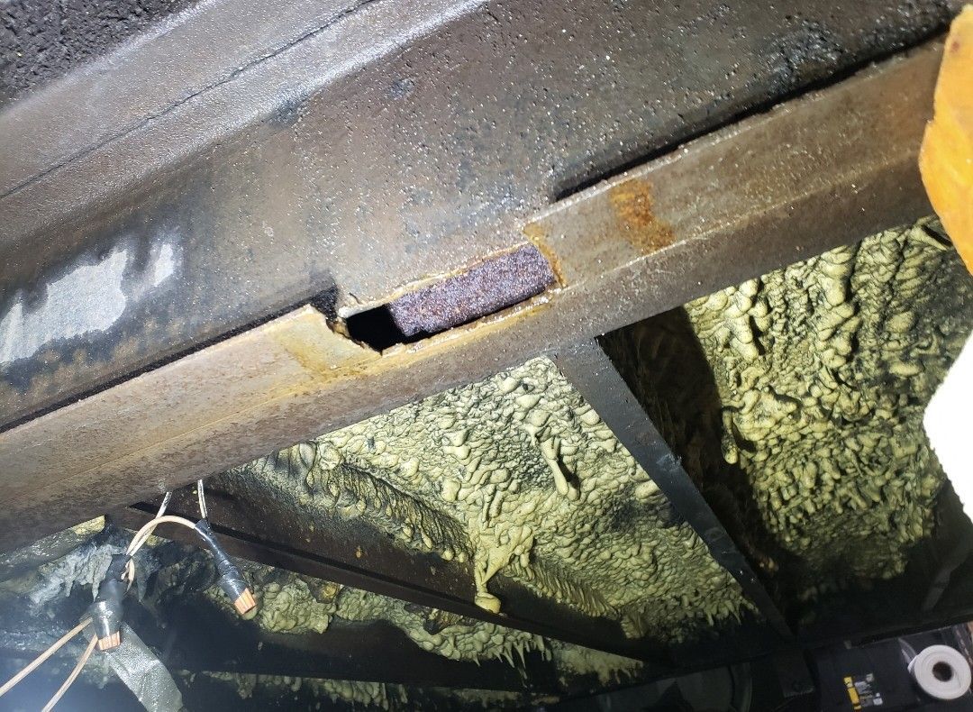 A metal structural beam shows a small rectangular cutout revealing purple insulation, with loose fiberglass nearby.