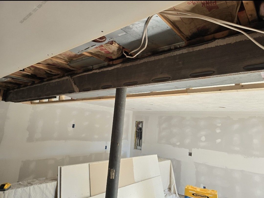 An interior view of a room under construction, showing an exposed steel beam and support post with unfinished drywall.