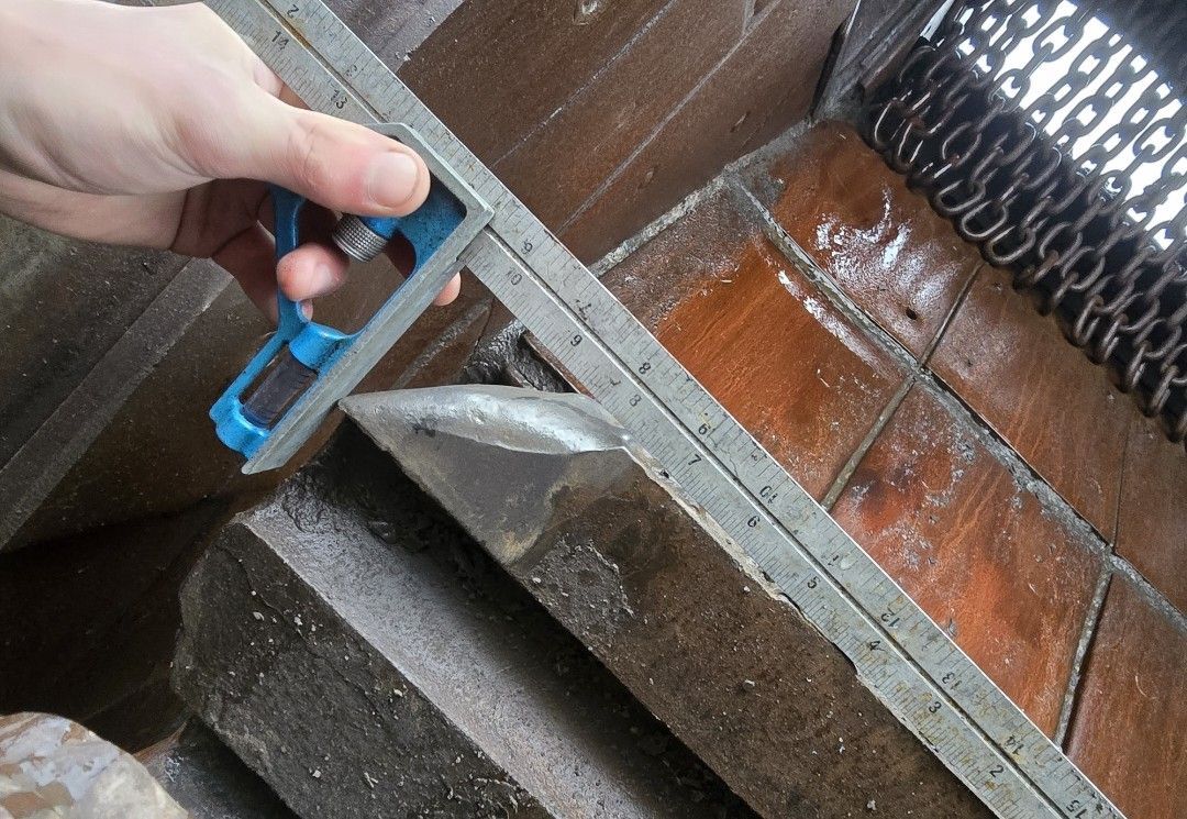 A hand uses a metal combination square to measure the angle and surface level of a block of stone in a workshop setting.
