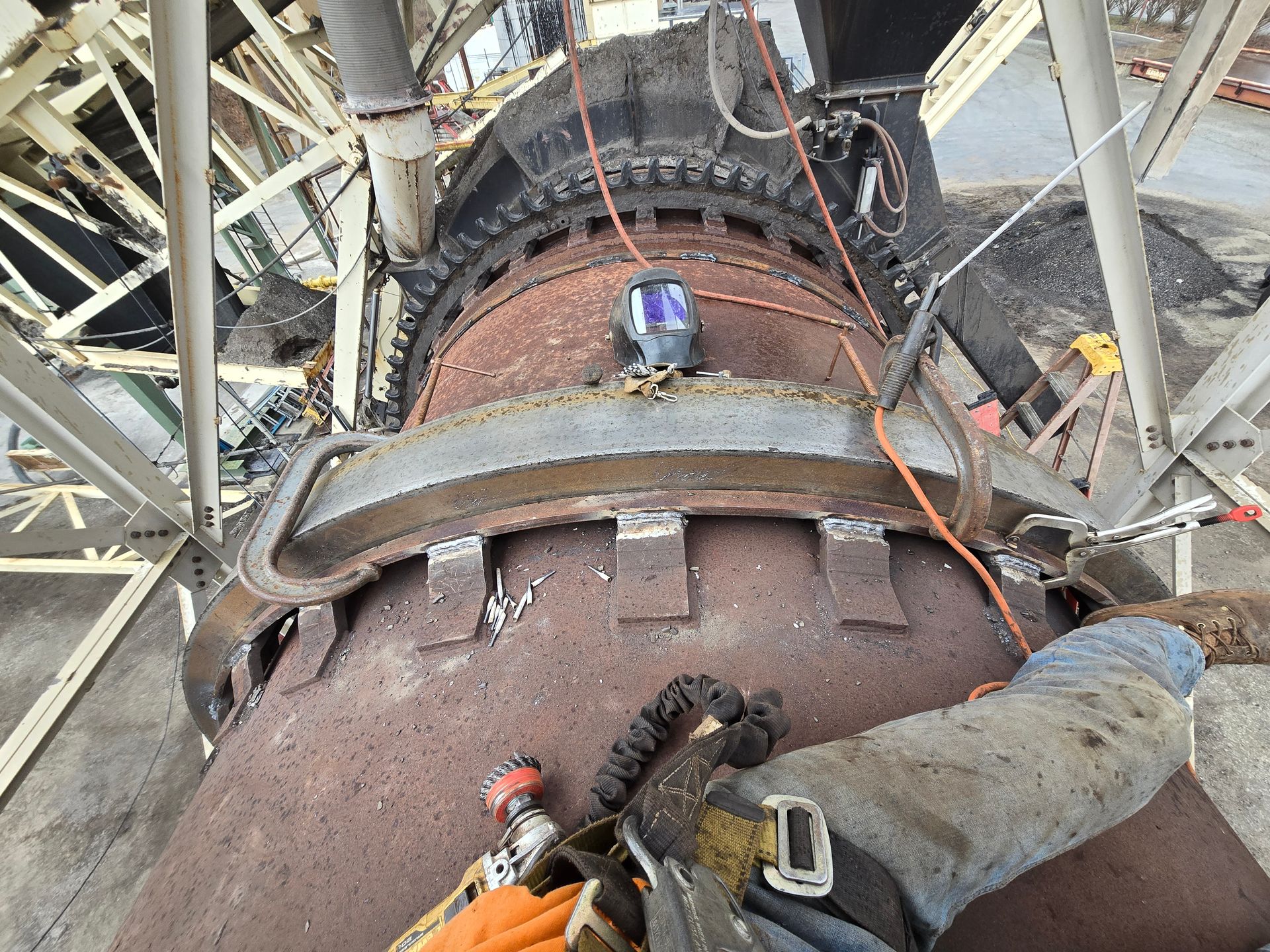Worker welding a large rusted industrial pipe