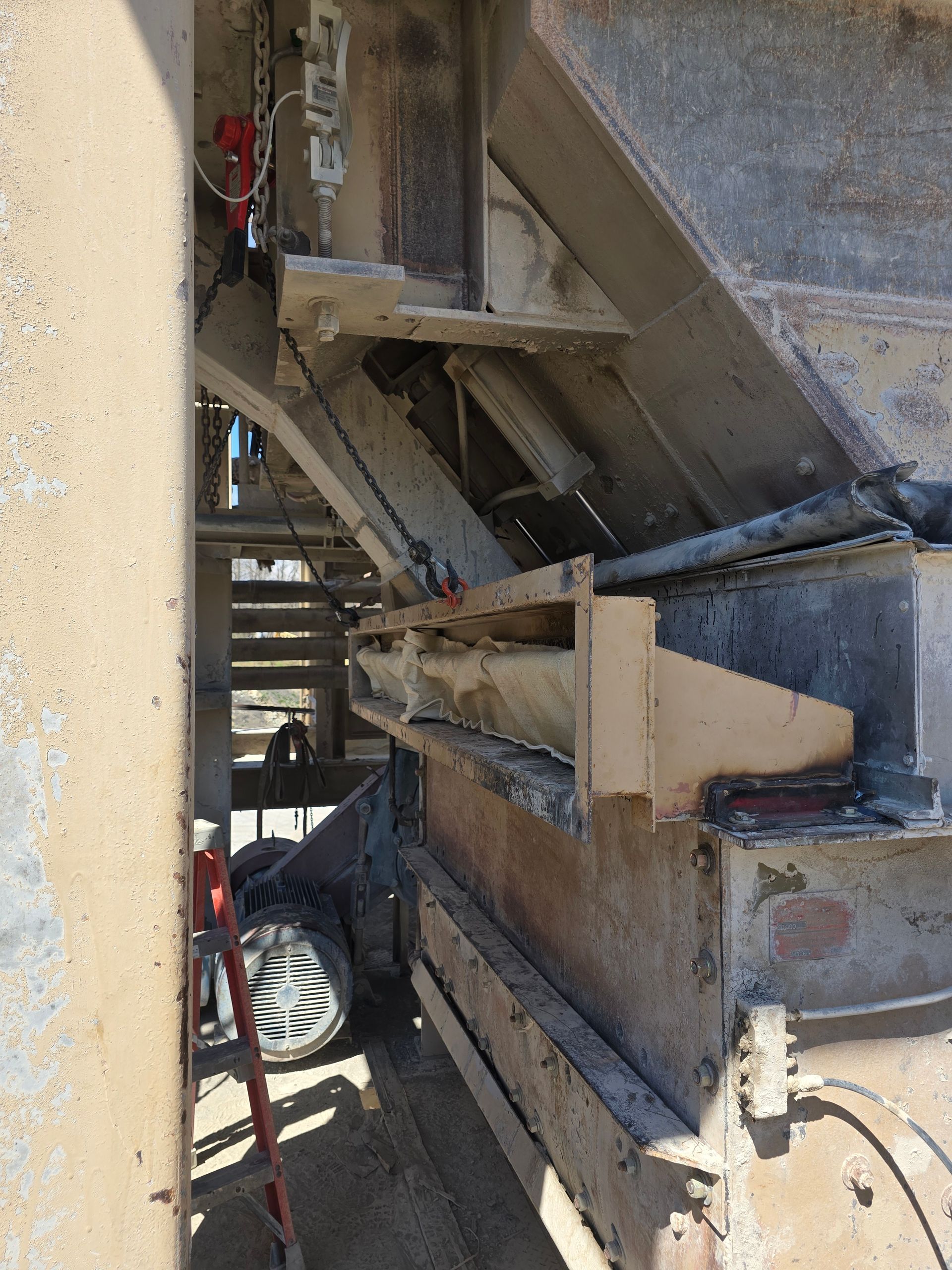 Dusty industrial conveyor machinery with metal framework and pipes under a structure