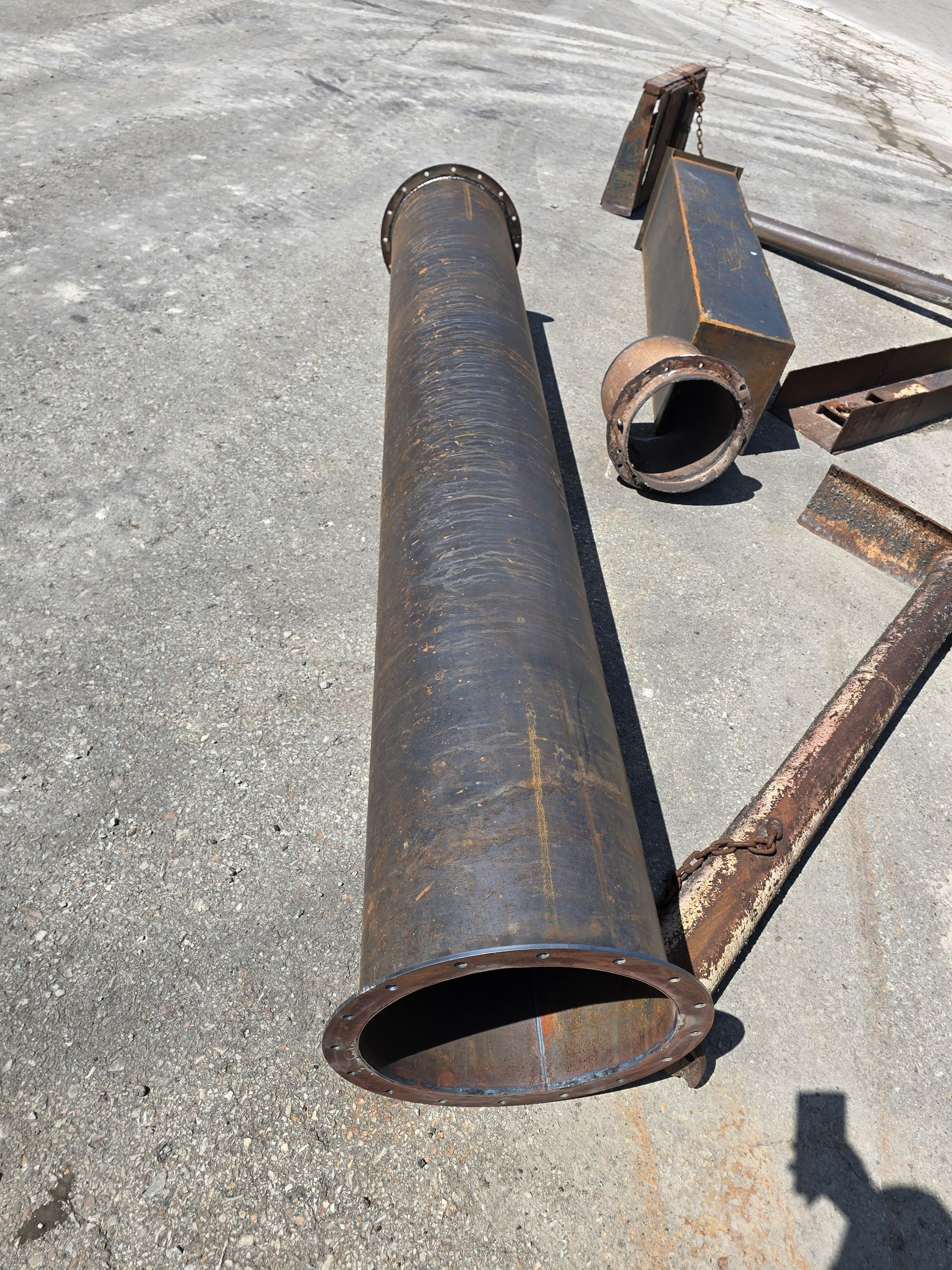 Rusty metal pipes and steel beams lying on a concrete surface outdoors