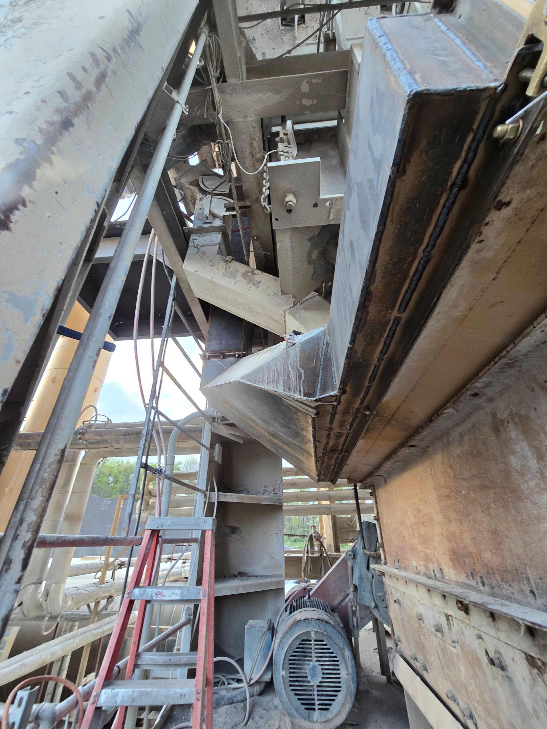 Industrial machinery and steel beams inside a narrow maintenance space, with a fan and ladder visible.