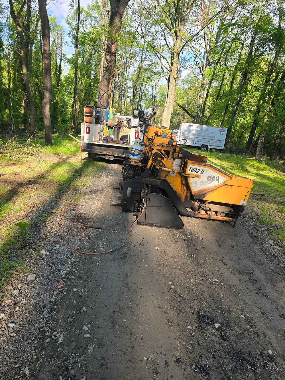 Road paving machine spreading fresh asphalt on a gravel forest road.