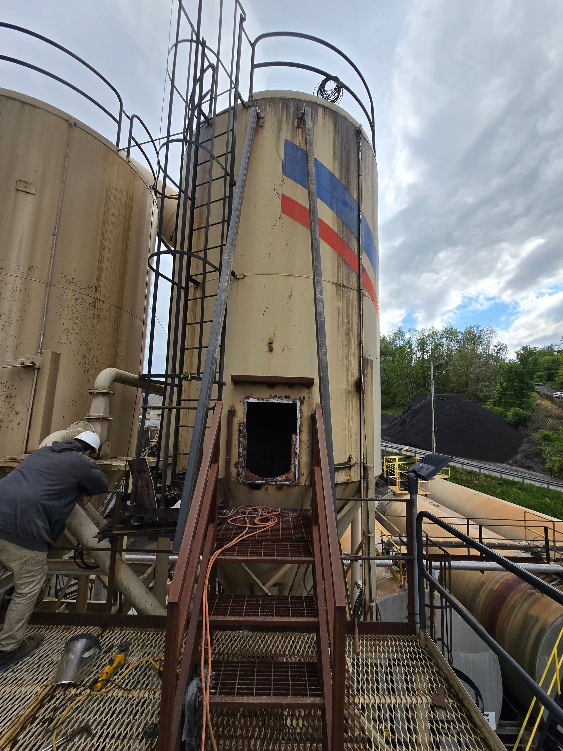 Worker beside tall industrial tanks and metal stairs on an outdoor factory site