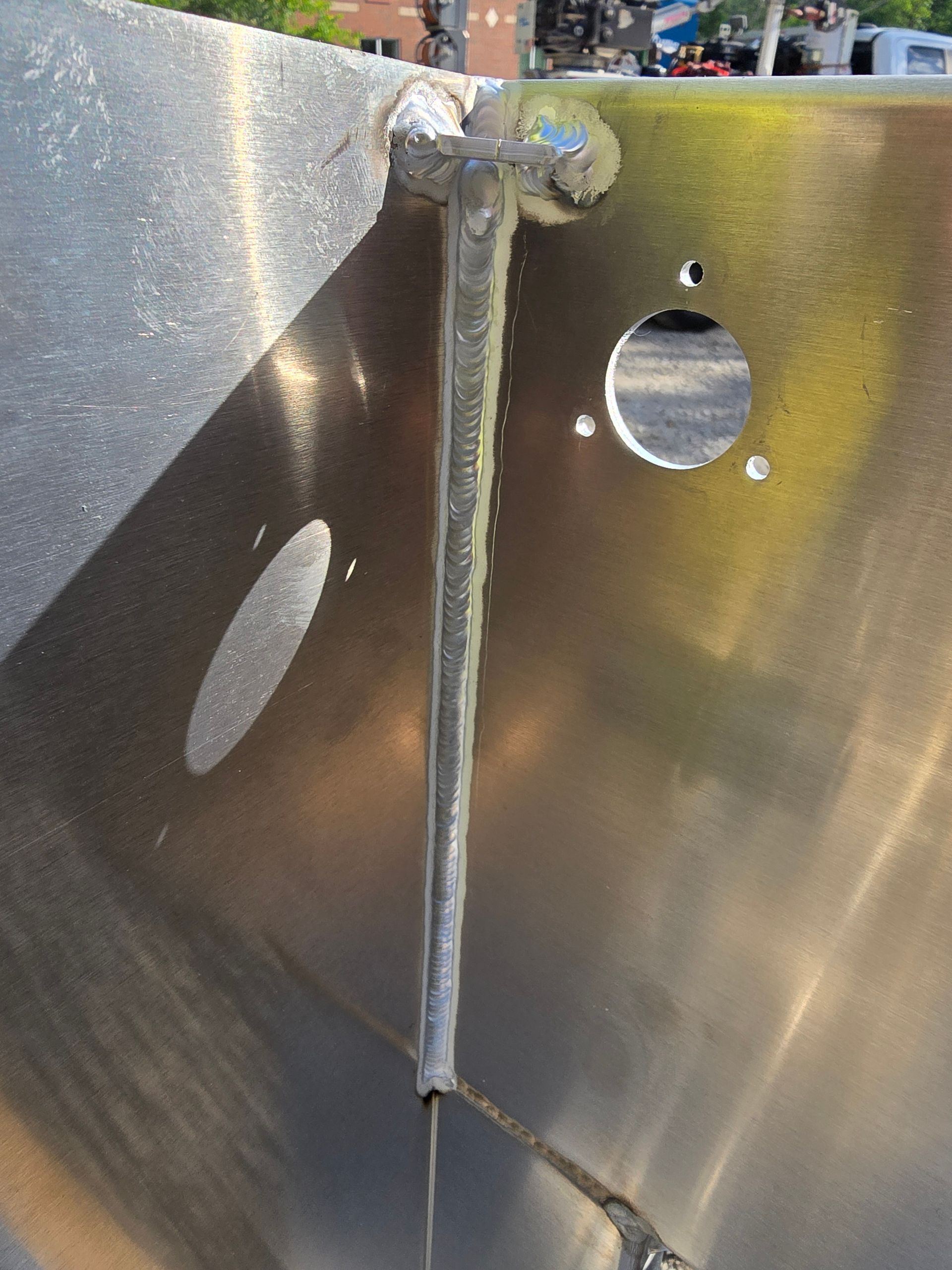 Close-up of a welded metal corner with two circular holes in brushed stainless steel.