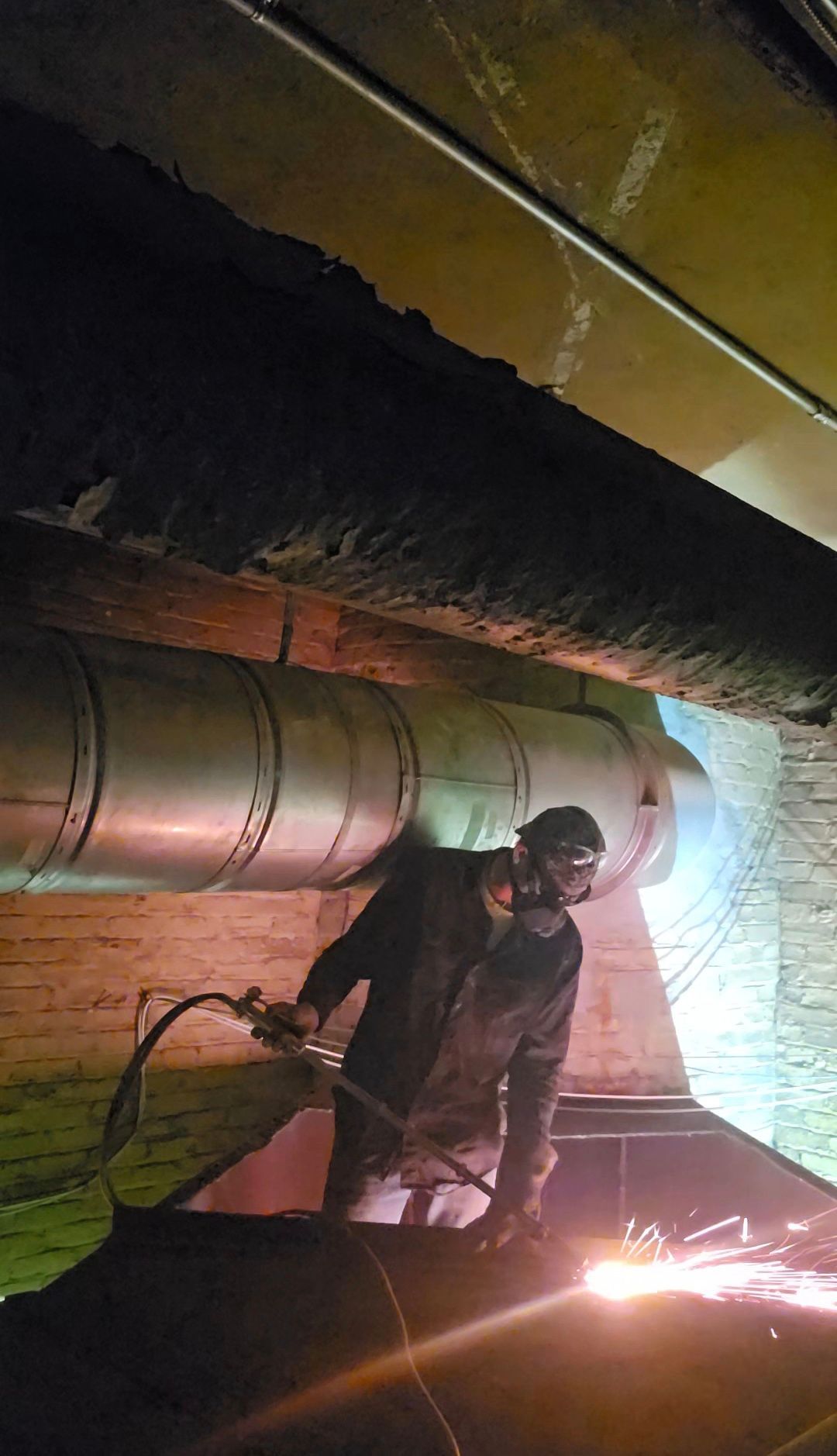 Worker welding inside a large metal pipe tunnel, with bright sparks and dark industrial surroundings.