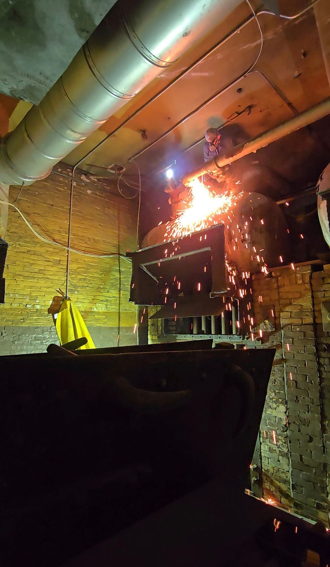 Worker in yellow jacket near a large indoor fire with sparks and smoke in an industrial setting