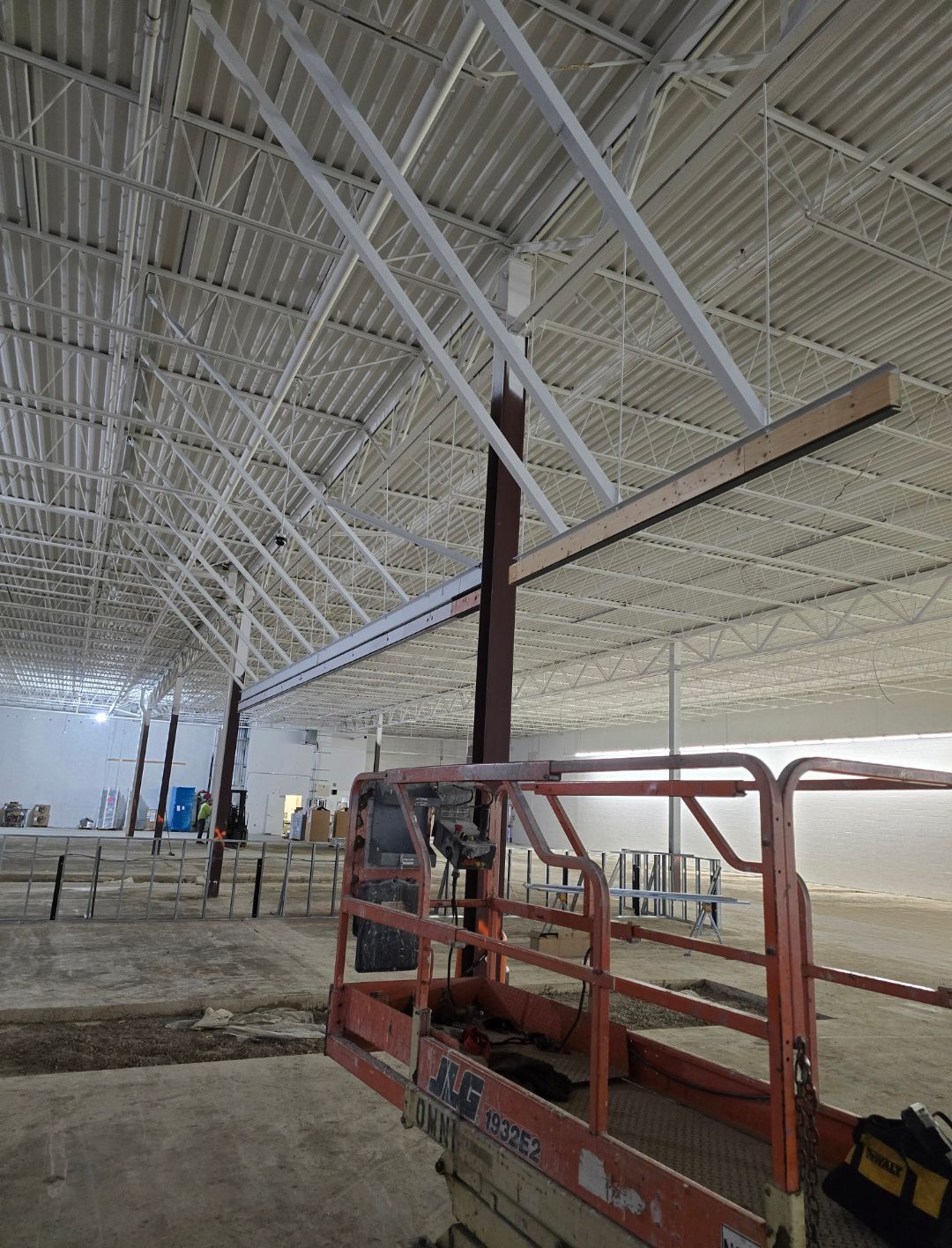 Red lift inside a large unfinished warehouse with white steel roof trusses and concrete floor
