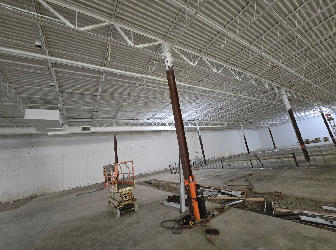 Empty industrial warehouse interior with exposed ceiling, scattered equipment, and unfinished concrete floor