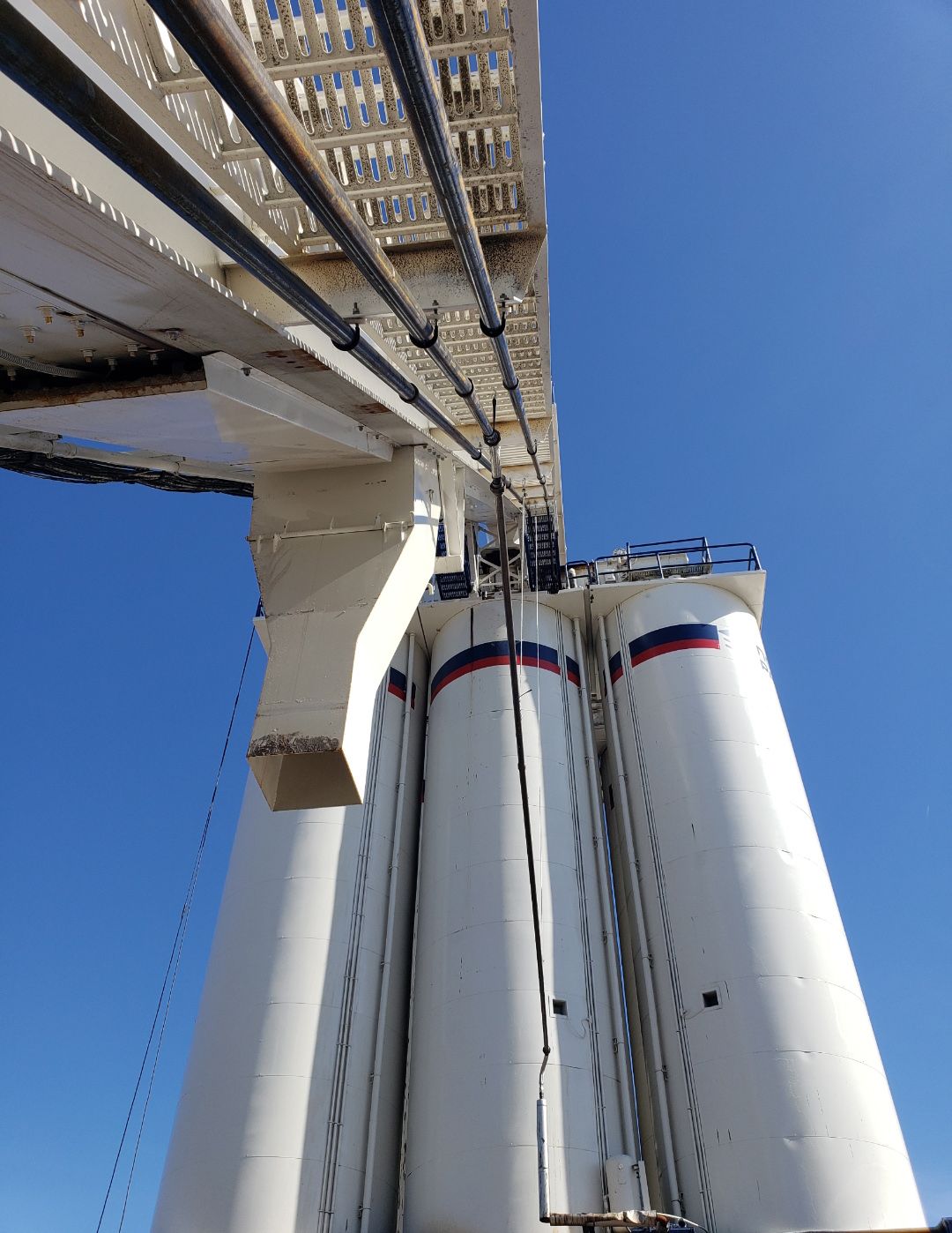 Tall white industrial silos under a metal conveyor against a blue sky
